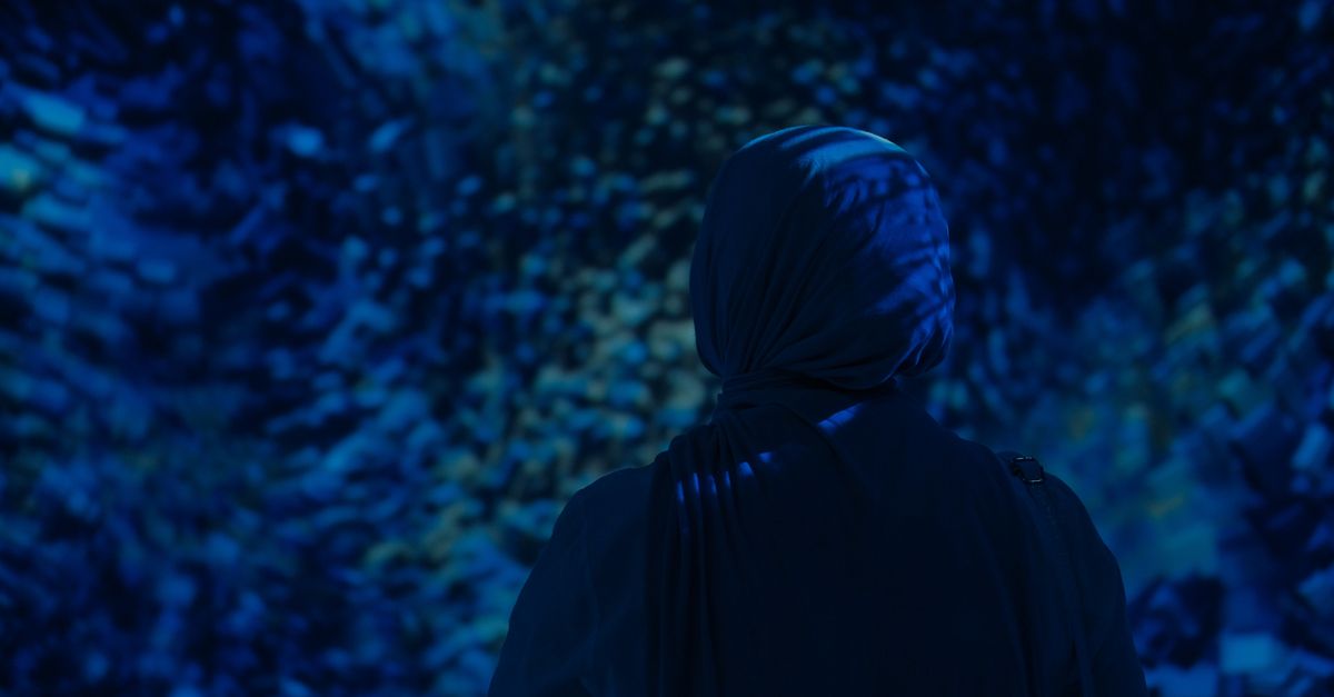Silhouetted woman in hijab stands against a dark, aquatic-themed background creating a serene and re