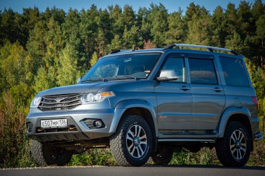 Silver SUV parked in a rural area surrounded by lush greenery, ideal for off-road adventures.