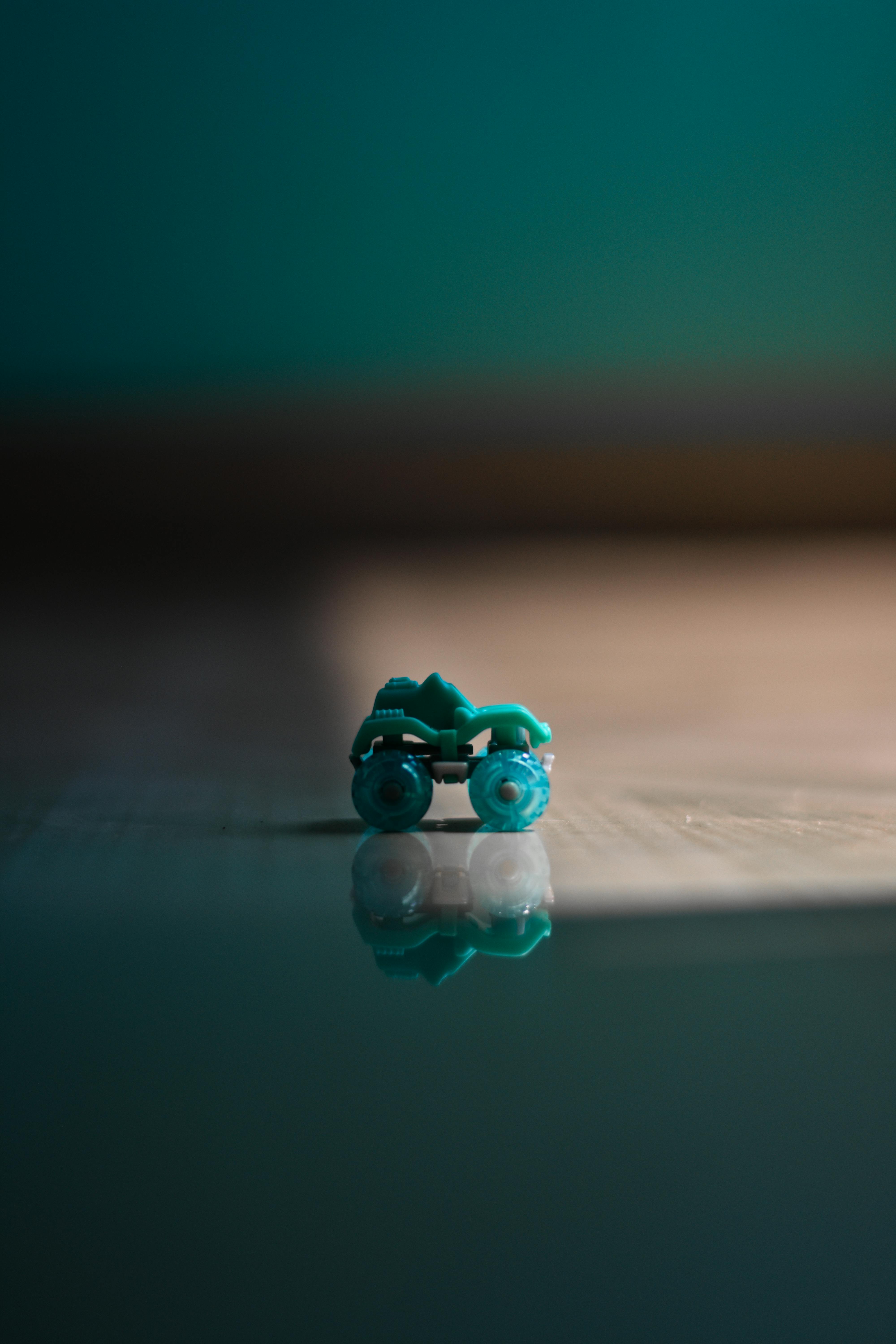 Minimalist photo of a green toy car on a reflective surface indoors.