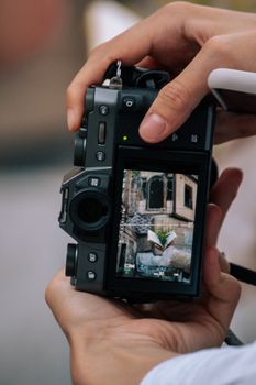 Hands holding a digital camera capturing an urban street scene.