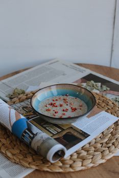 A bowl of creamy porridge topped with red berries, set on a magazine for a stylish breakfast scene.