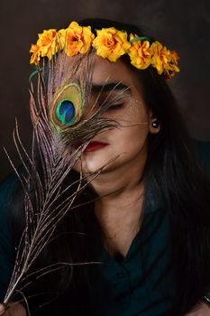 A creative portrait of a woman with a floral wreath and peacock feather, eyes closed.