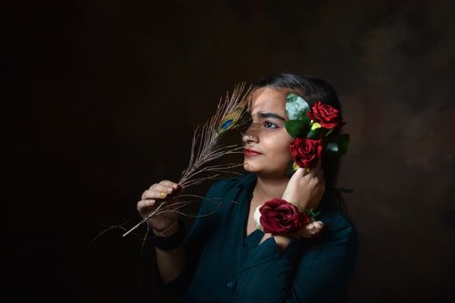 Free A thoughtful portrait of a woman adorned with roses and a peacock feather, showcasing elegance and beauty. Stock Photo