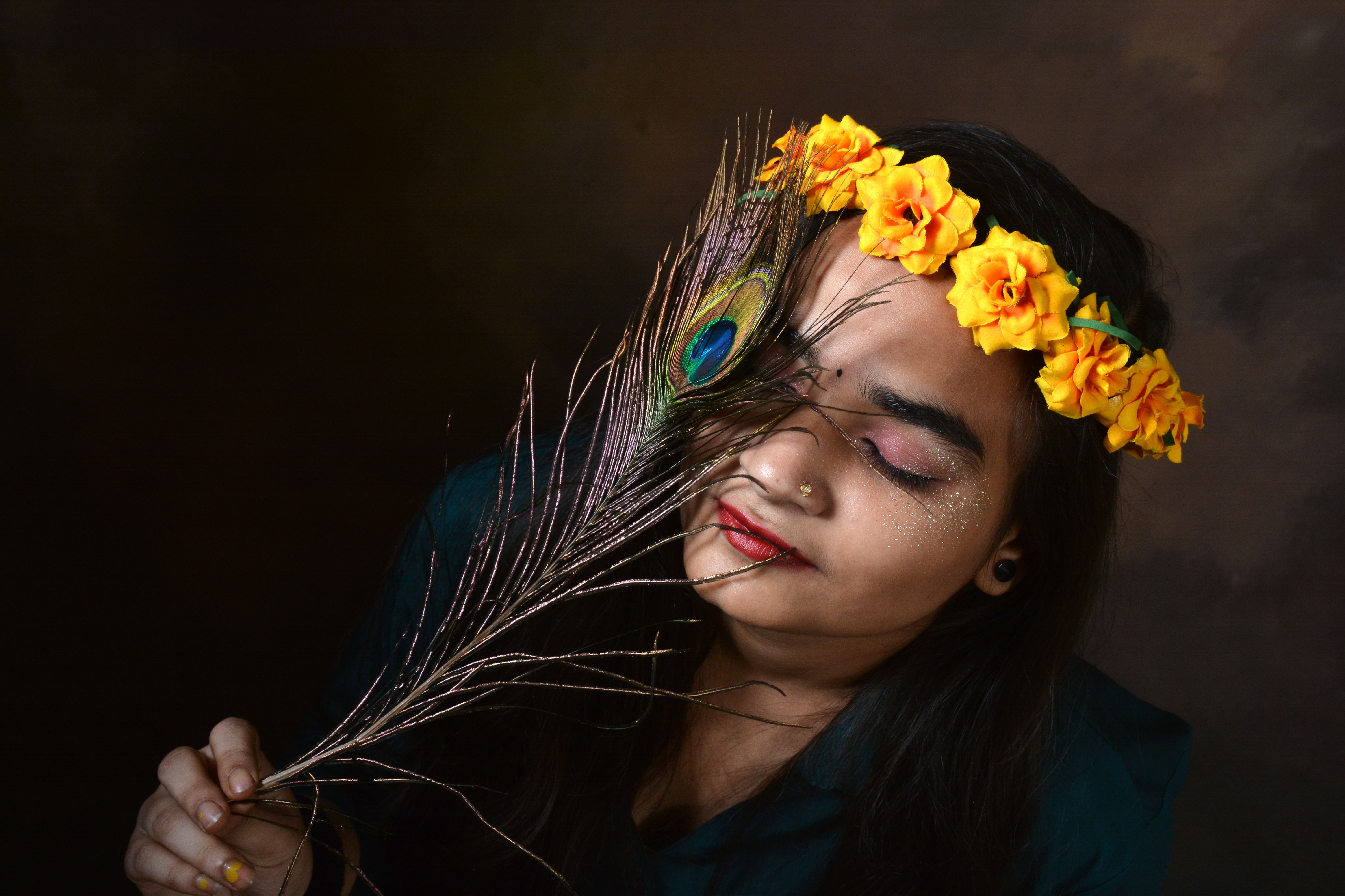 A woman adorned with a floral crown holds a peacock feather, embodying grace and cultural beauty.