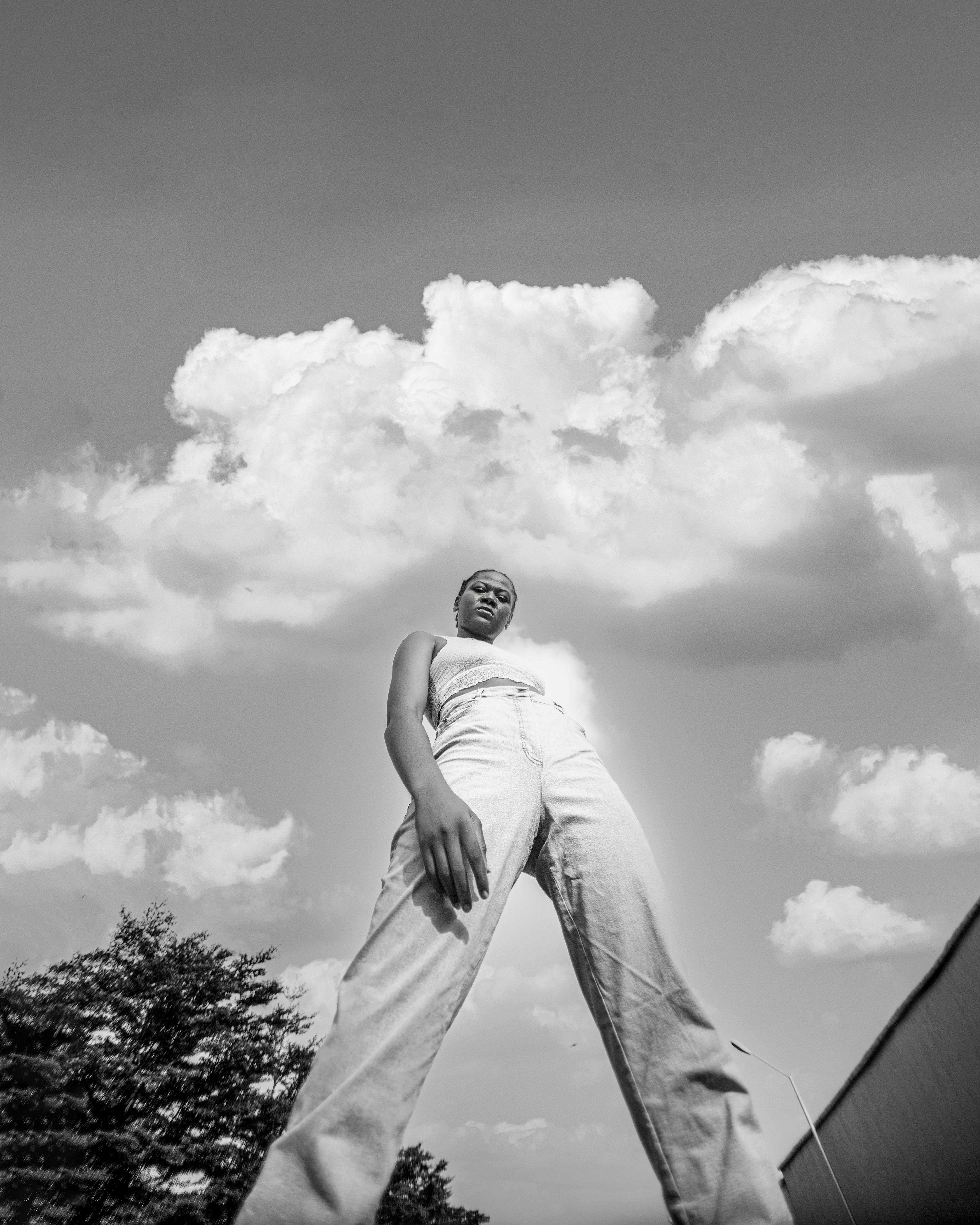 Elegant black and white street portrait of a woman posing under a dynamic sky.