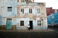 A weathered building with a man sitting outside in the urban streets of Mindelo, Cape Verde.