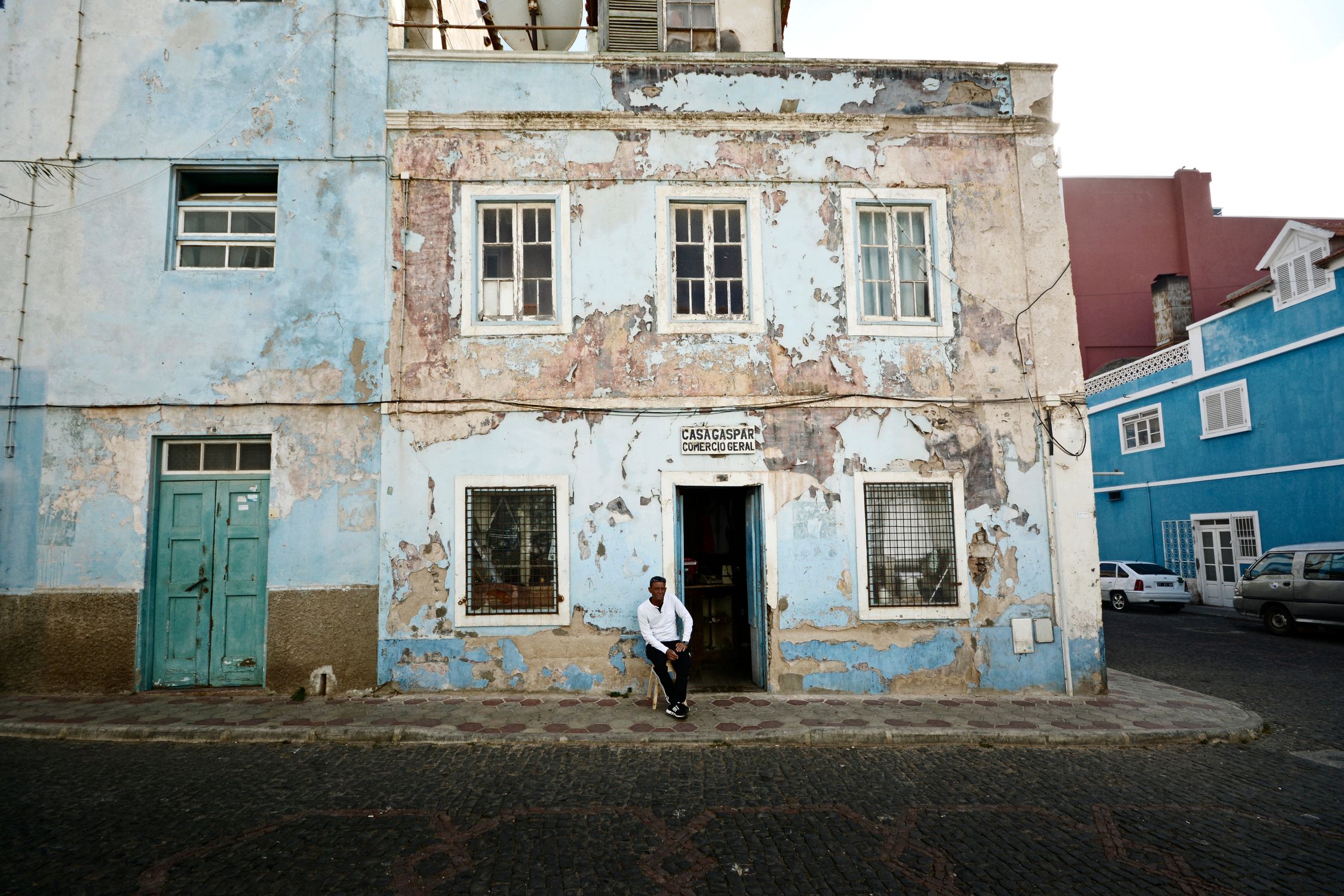 A weathered building with a man sitting outside in the urban streets of Mindelo, Cape Verde.