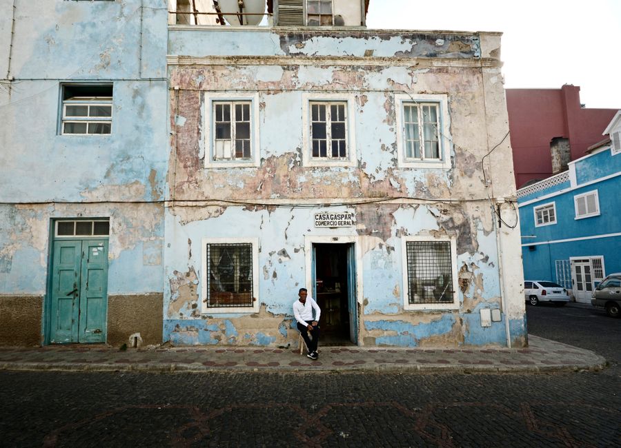 A weathered building with a man sitting outside in the urban streets of Mindelo, Cape Verde.