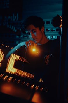 A young man in a dark room illuminated by moody neon lights, reflecting introspection.