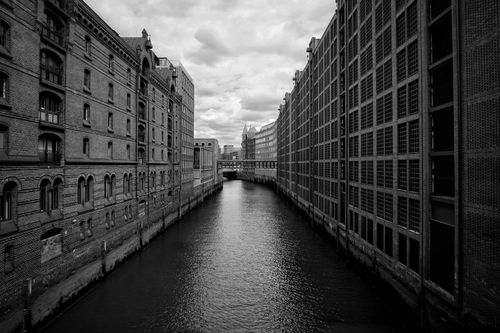 Free Monochrome view of an urban canal flanked by symmetrical postindustrial architecture under overcast skies. Stock Photo