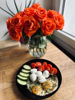 Delicious breakfast of eggs and mozzarella with vibrant red roses in a vase on a wooden table.