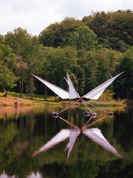 A tranquil lake with a mirrored sculpture and forest backdrop, captured in natural light.
