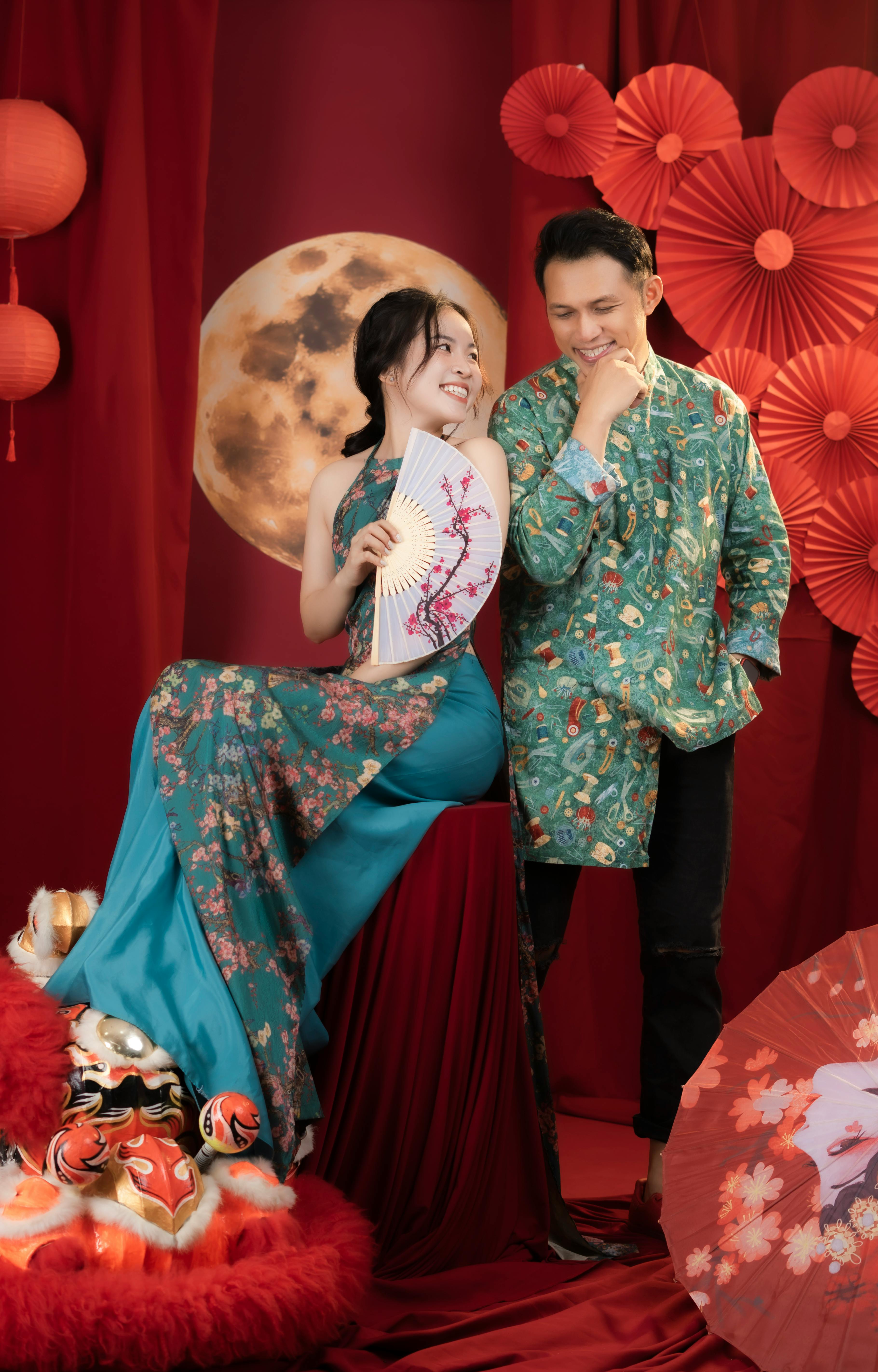 Asian couple in colorful traditional costumes with festive decorations and fan.