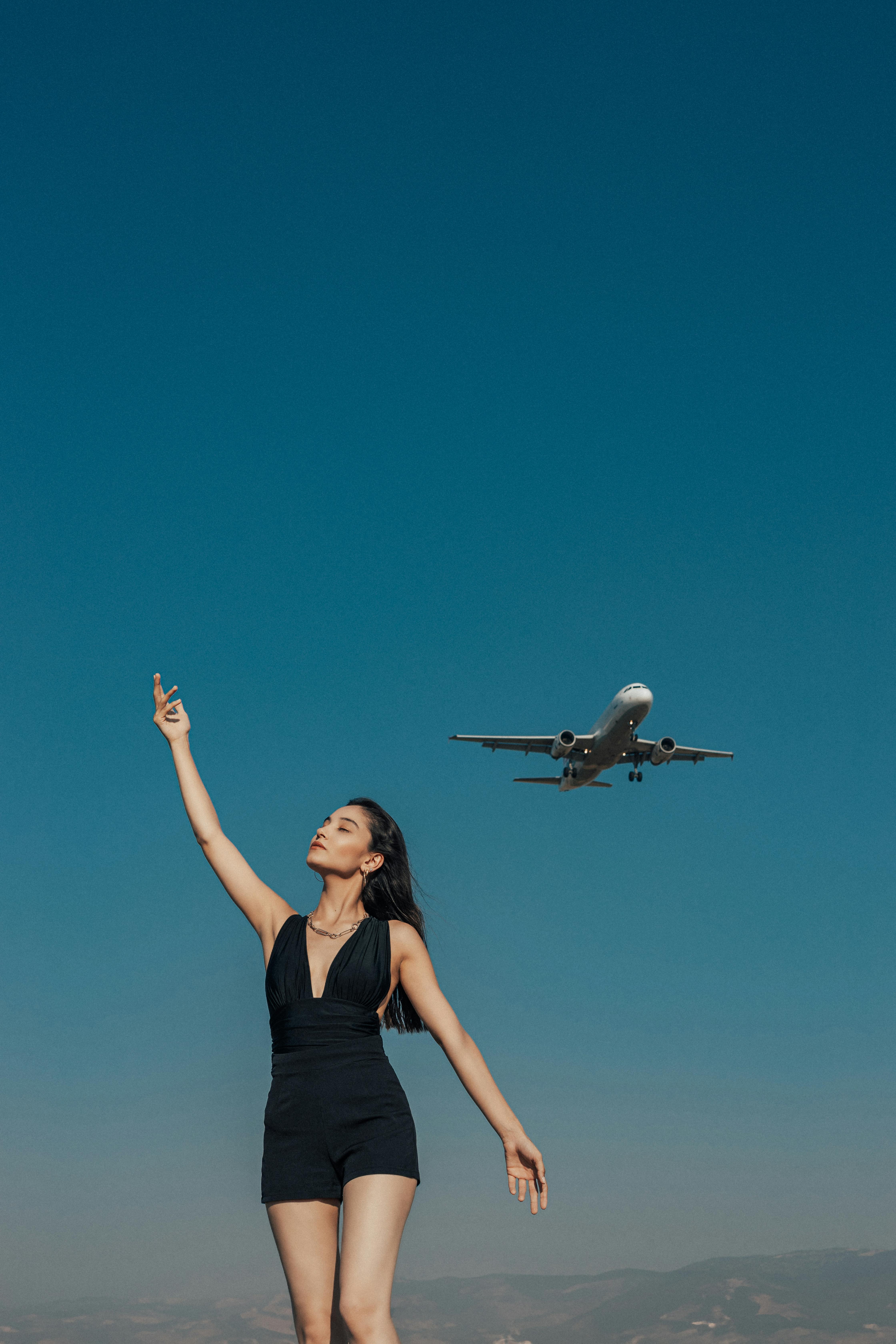 A woman enjoying a sunny day outdoors with an airplane flying overhead in Kahramanmaraş, Türkiye.