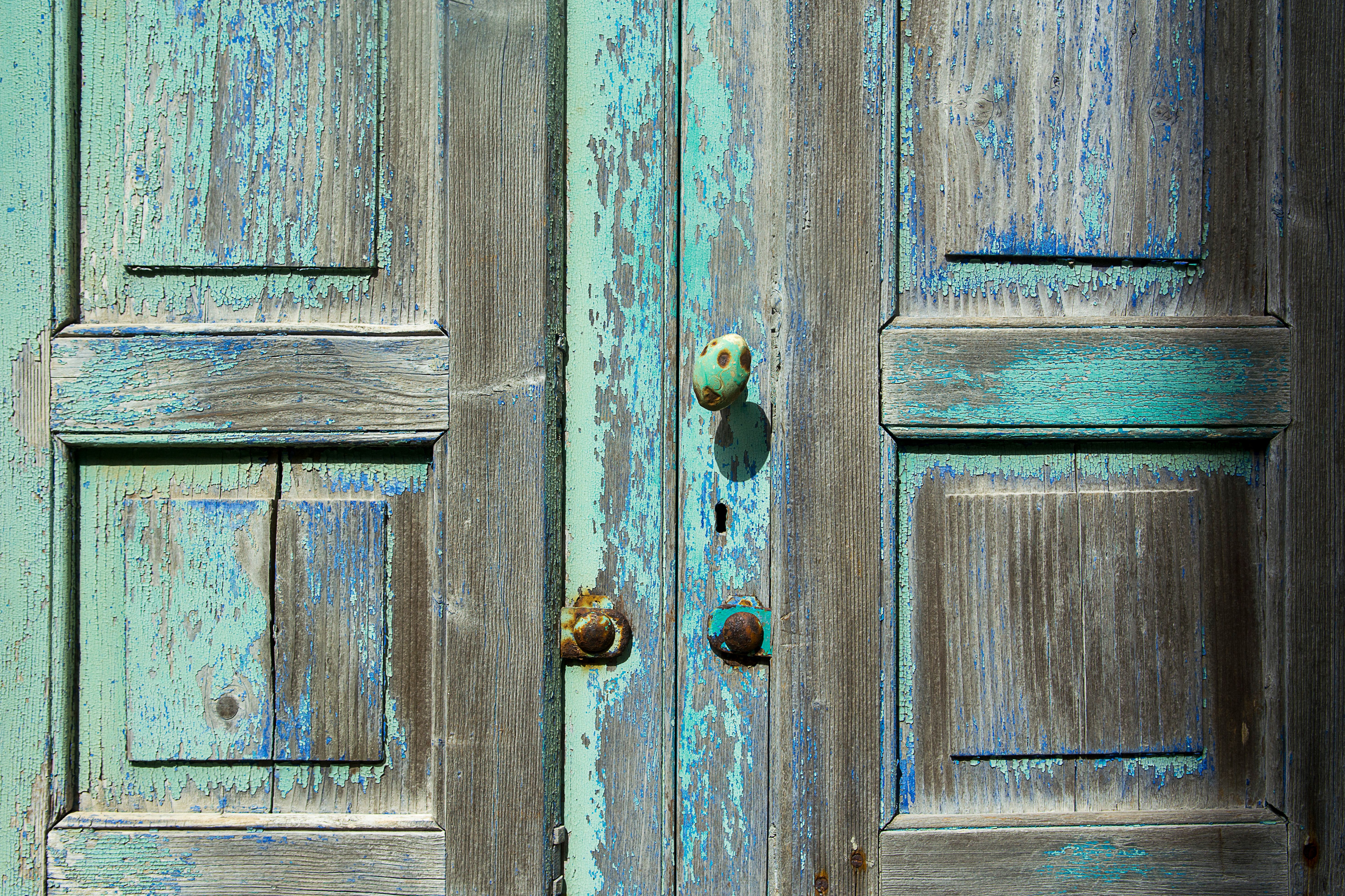 Close-up of weathered wooden doors showcasing rustic blue and turquoise paint texture with vintage doorknob.
