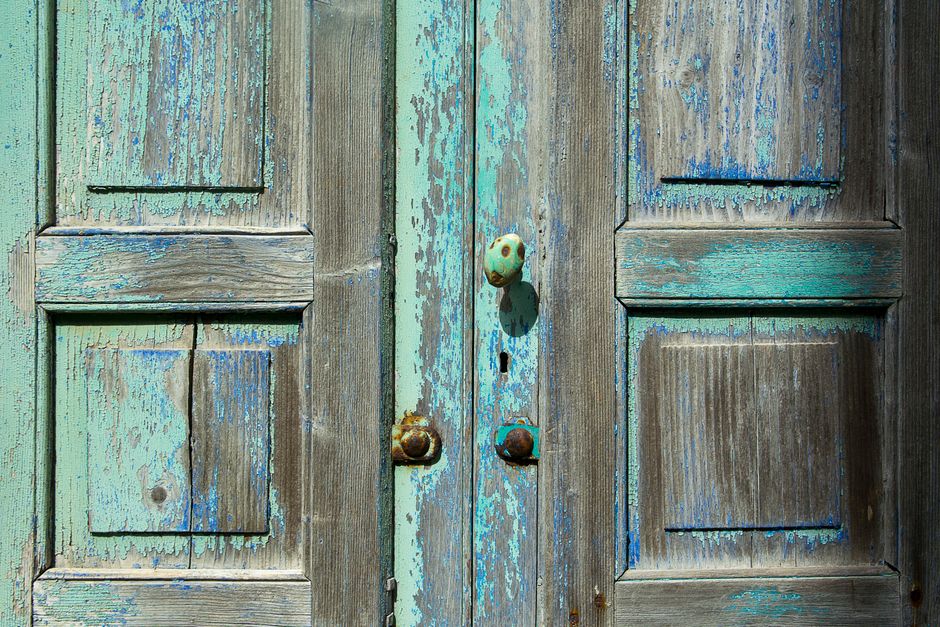 Close-up of weathered wooden doors showcasing rustic blue and turquoise paint texture with vintage doorknob.