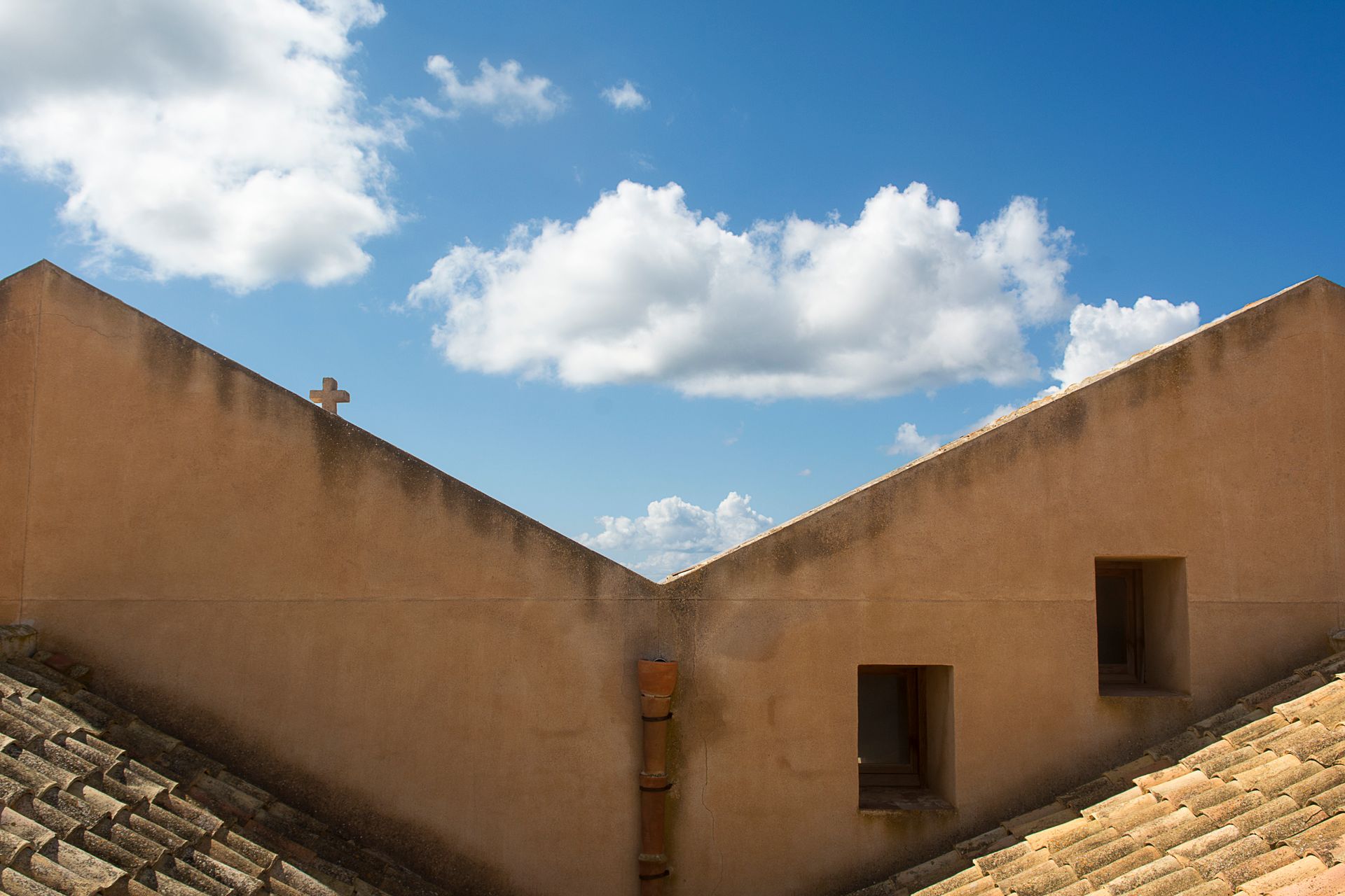 A rooftop with clay tiles under a clear blue sky with scattered clouds.
