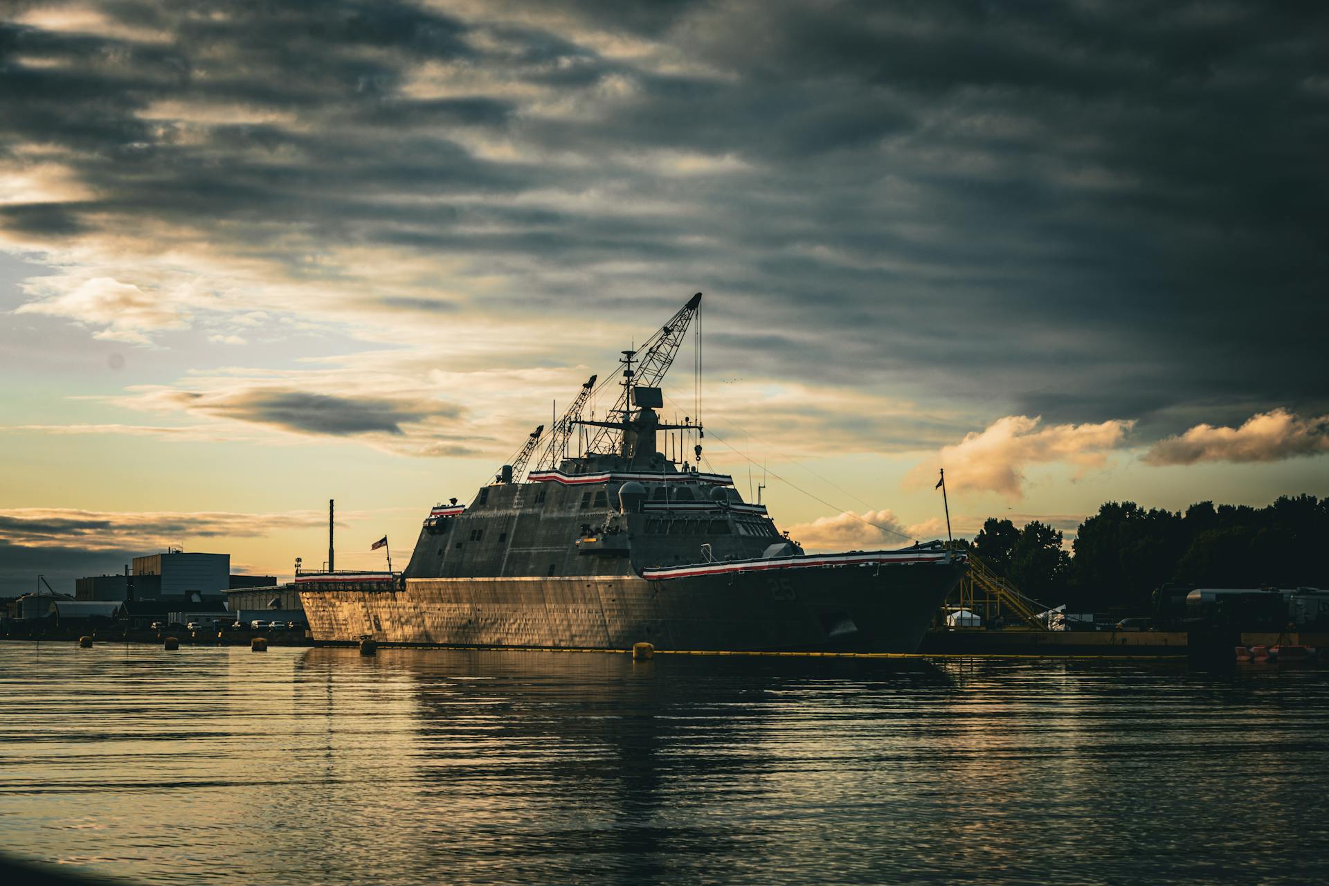 A military vessel docked at Marinette Harbor during a dramatic sunset with overcast clouds.
