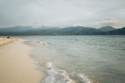 Free Tranquil beachfront landscape with serene ocean and mountain backdrop, perfect for a peaceful escape. Stock Photo
