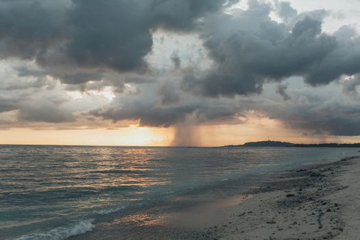 An awe-inspiring sunset over a cloudy beach with striking ocean views and distant rain.