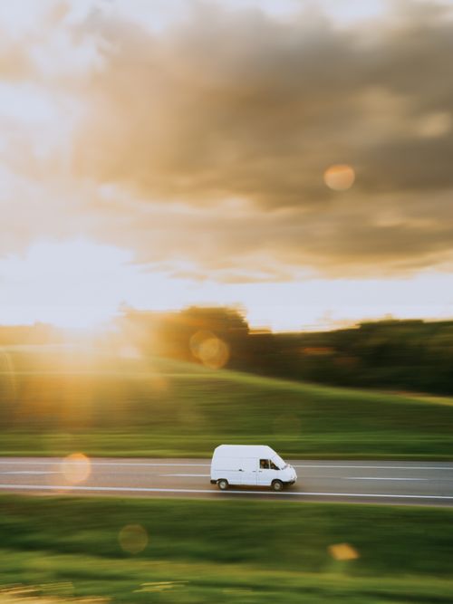 Free White van driving fast on a countryside road during a golden sunset with motion blur. Stock Photo