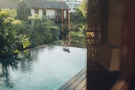 一只猴子在游泳池边漫步，四周环绕着郁郁葱葱的热带植物和现代建筑，显得宁静祥和