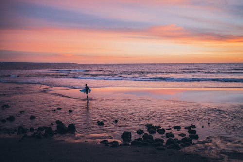 Person Standing On Shore Holding Surfboard