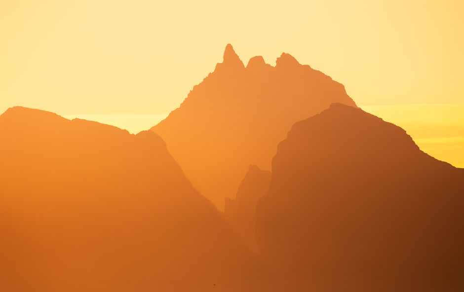 Majestic Lofoten peaks silhouetted at sunset in a warm golden haze, Norway's tranquil beauty.
