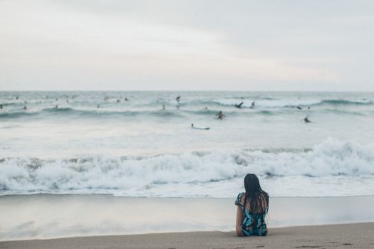 一名妇女坐在海滩上，观看海浪中的冲浪者