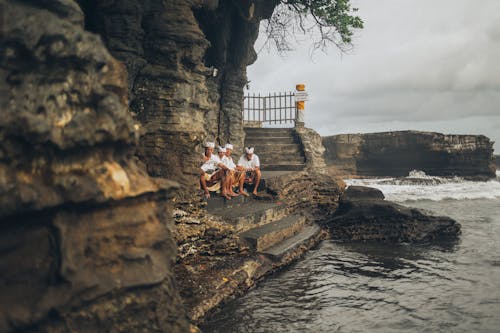 Free Four Men Sitting on Stairs Front of Body of Water Stock Photo