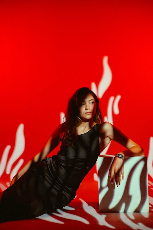 Studio Shot of a Young Woman in a Black Dress on Red Background 
