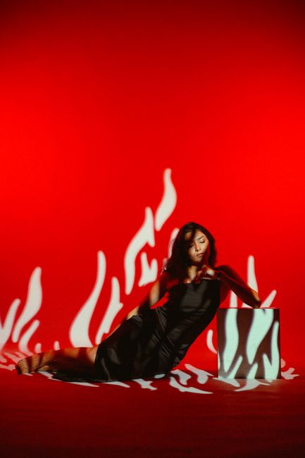 Young woman in a black dress posing against a vibrant red backdrop with artistic shadows in a studio setting.