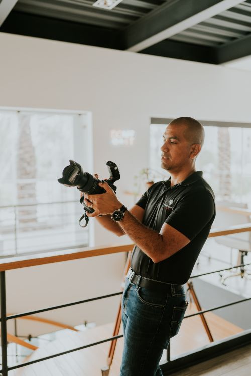 Free A professional photographer holding a modern camera indoors, preparing for a shot. Stock Photo