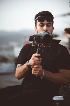 A young man holding a camera outdoors, focusing on capturing moments with precision.