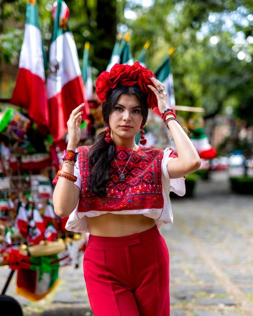 Free Young woman in traditional Mexican dress posing outdoors with flags, celebrating culture. Stock Photo