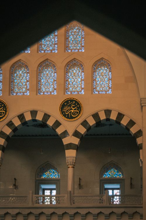 Free A serene view of a mosque's interior with detailed arches and stained glass windows. Stock Photo