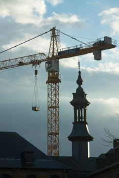 A construction crane towers over historic architecture against a cloudy sky, blending modernity with tradition.