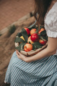 A woman sitting outdoors holding a basket of fresh red apples, evoking a sense of pastoral tranquility.