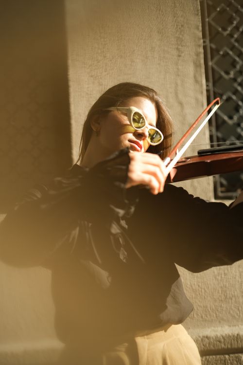 Free A young female violinist wearing sunglasses plays passionately on a street in Ankara at sunset. Stock Photo