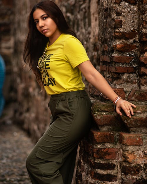 Young Woman in Yellow T-Shirt and Khaki Cargo Pants Posing by a Brick Wall