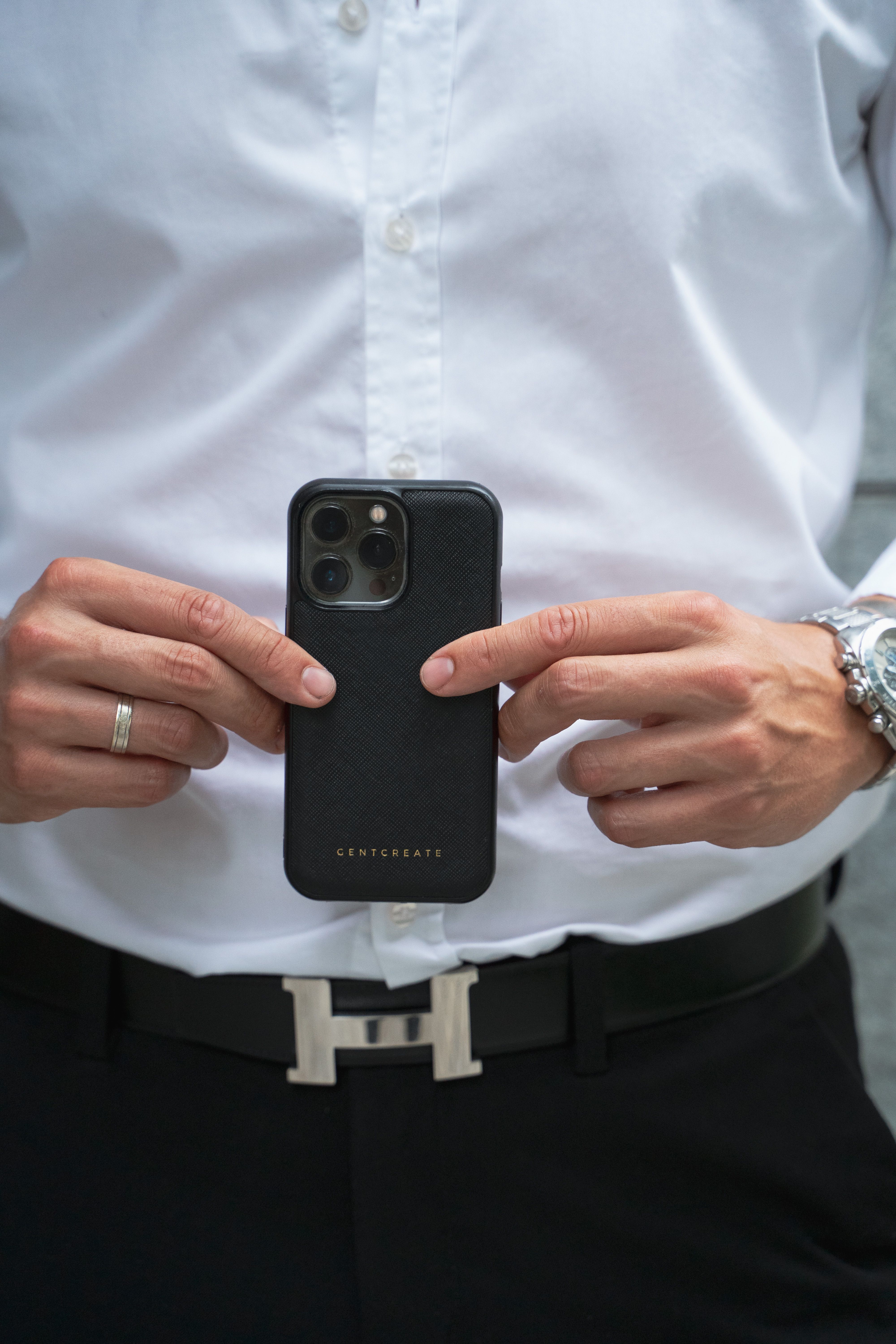 Close-up of a man holding a smartphone in a stylish black case, showcasing fashion and technology.