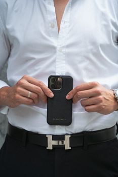 Close-up of a man holding a smartphone with a leather case, showcasing fashion and technology.