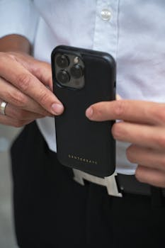 Detailed image of hands holding a modern smartphone, featuring a black case with a metallic belt.
