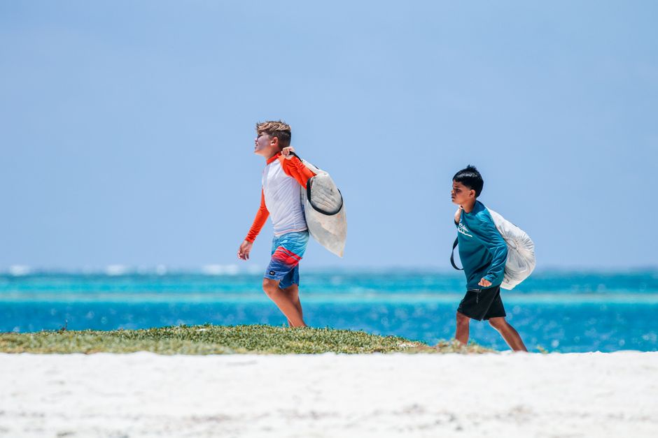 Two boys walk on a sunny beach carrying surfboards, enjoying a peaceful vacation day by the ocean.