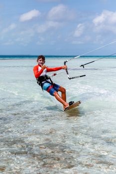 Teenager kiteboarding in clear ocean waters under a sunny sky, enjoying summer vacation.
