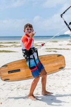 Teen boy enjoying a sunny beach day with a kiteboard, making a Shaka gesture.