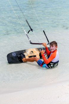 Teenager enjoying kitesurfing on a tropical beach, showcasing skills with a relaxed pose.