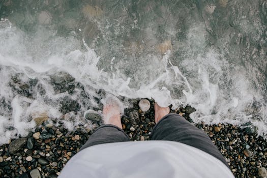 View of bare feet standing on a pebble beach with ocean waves.
