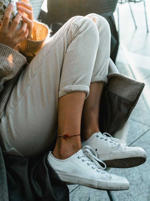 Close-up of a person sitting comfortably with white sneakers and a colorful anklet