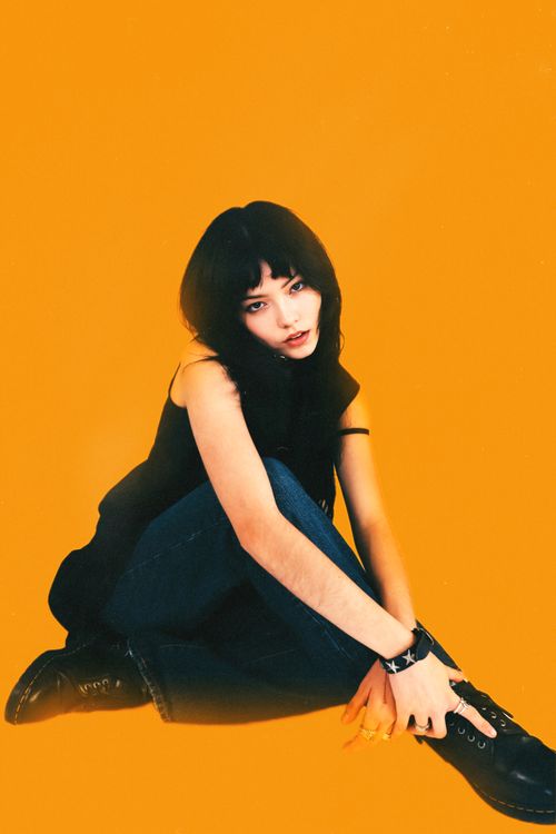 Free Stylish woman posing in studio with vibrant orange background wearing fashion-forward attire. Stock Photo